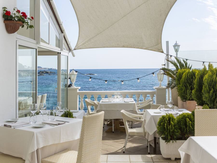 Une terrasse avec des tables dressées pour le dîner, offrant une vue sur la mer.