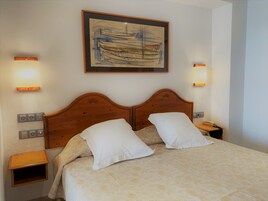 Una cama bien hecha con una colcha estampada, dos almohadas blancas y un cabecero de madera. Hay dos mesitas de noche con lámparas, un enchufe de pared y una obra de arte enmarcada sobre la cama.
