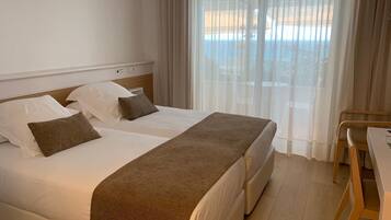Habitación de hotel con cama, escritorio y vista al mar a través de cortinas traslúcidas.
