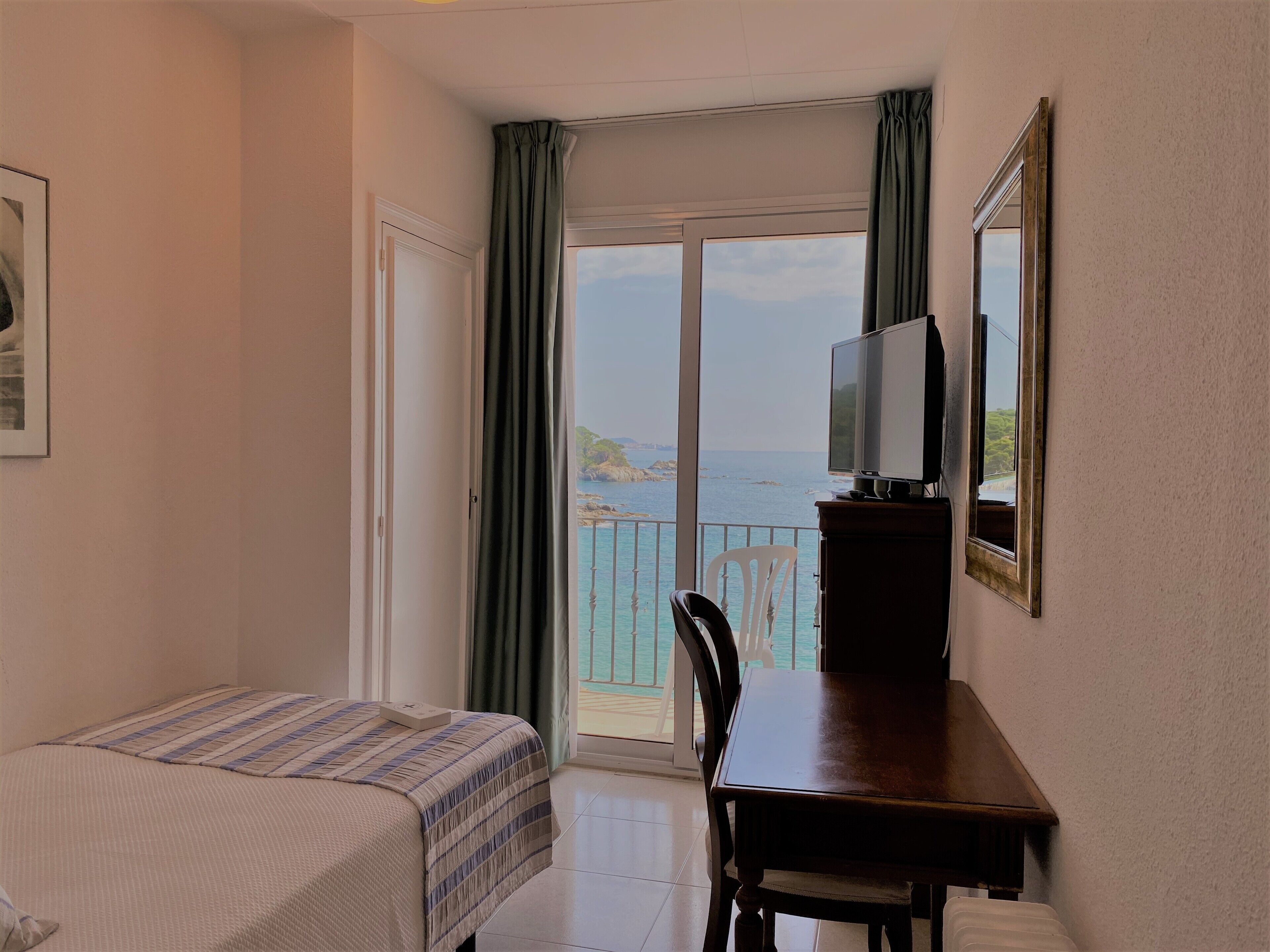 Habitació d'hotel amb llit, escriptori amb televisió i balcó que fa a la mar.