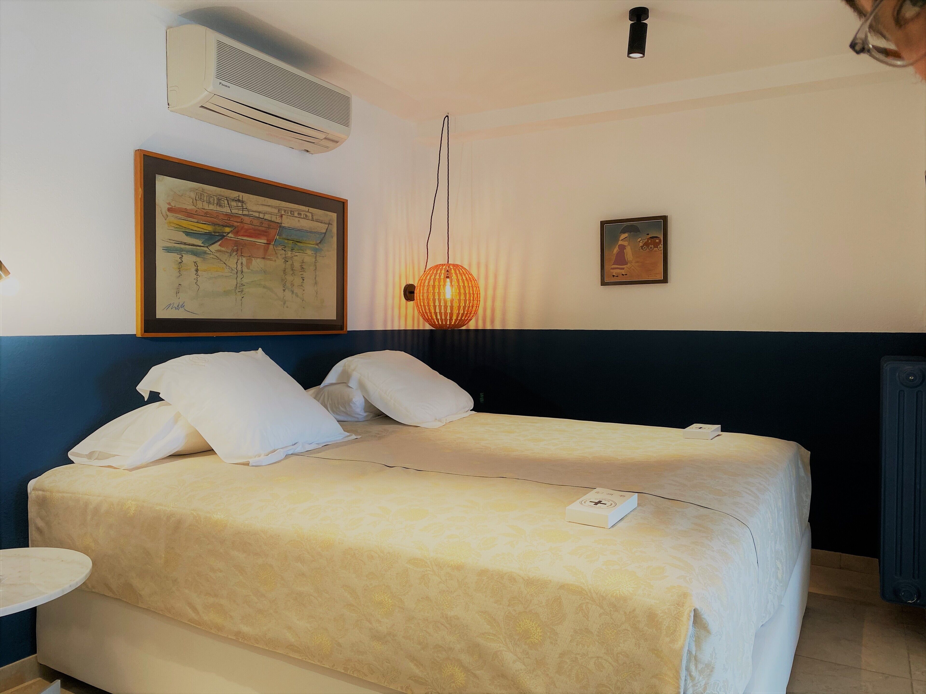 Habitación de hotel con cama, una mesa redonda, aire acondicionado de pared y dos cuadros enmarcados.