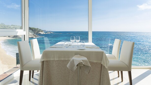 Una mesa de comedor con vista al mar, sillas blancas y un mantel.
