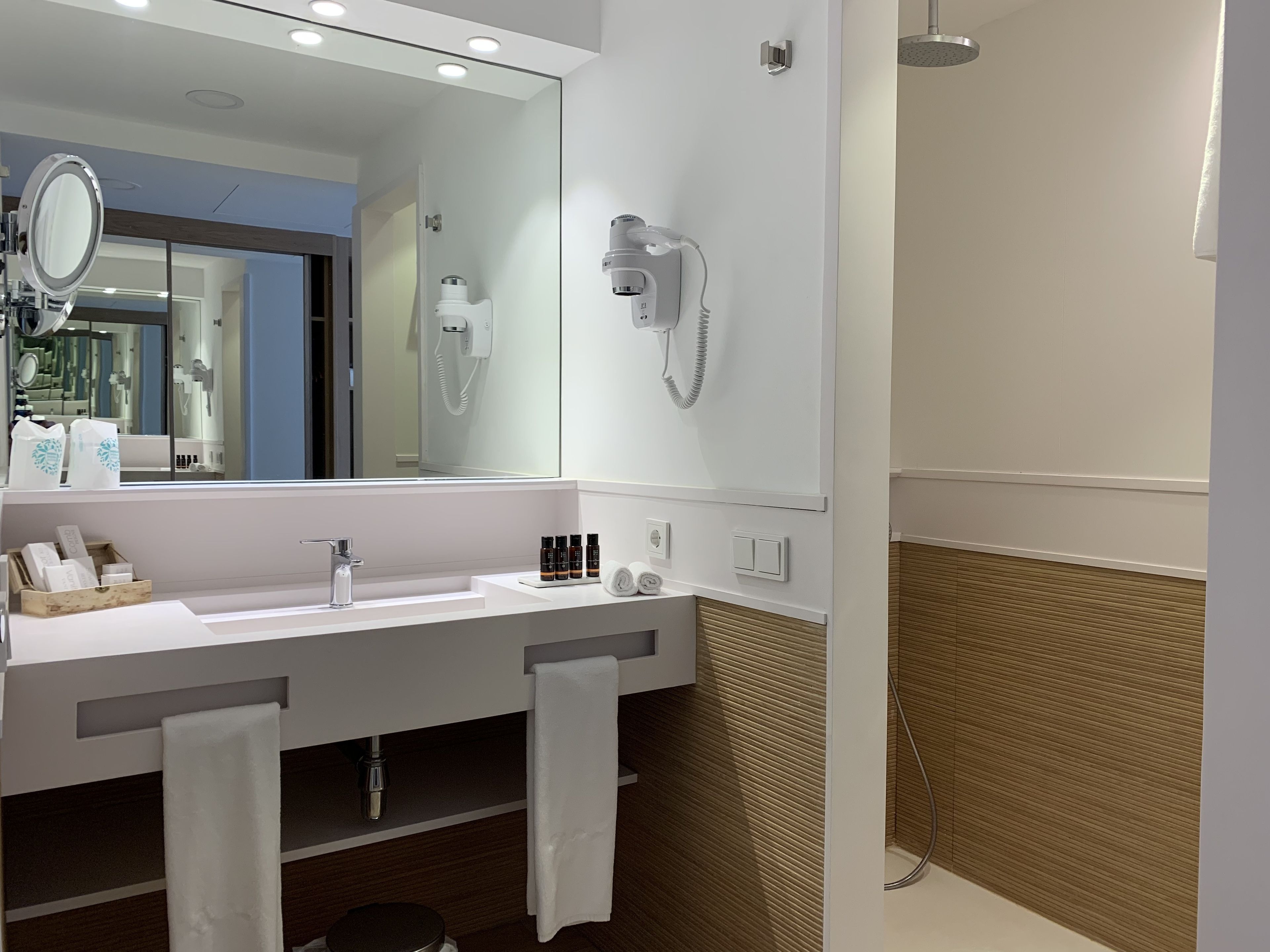 A modern bathroom with a large mirror, two sinks, a hairdryer, and a towel rack.