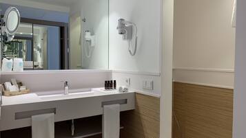 A modern bathroom with a large mirror, two sinks, a hairdryer, and a towel rack.