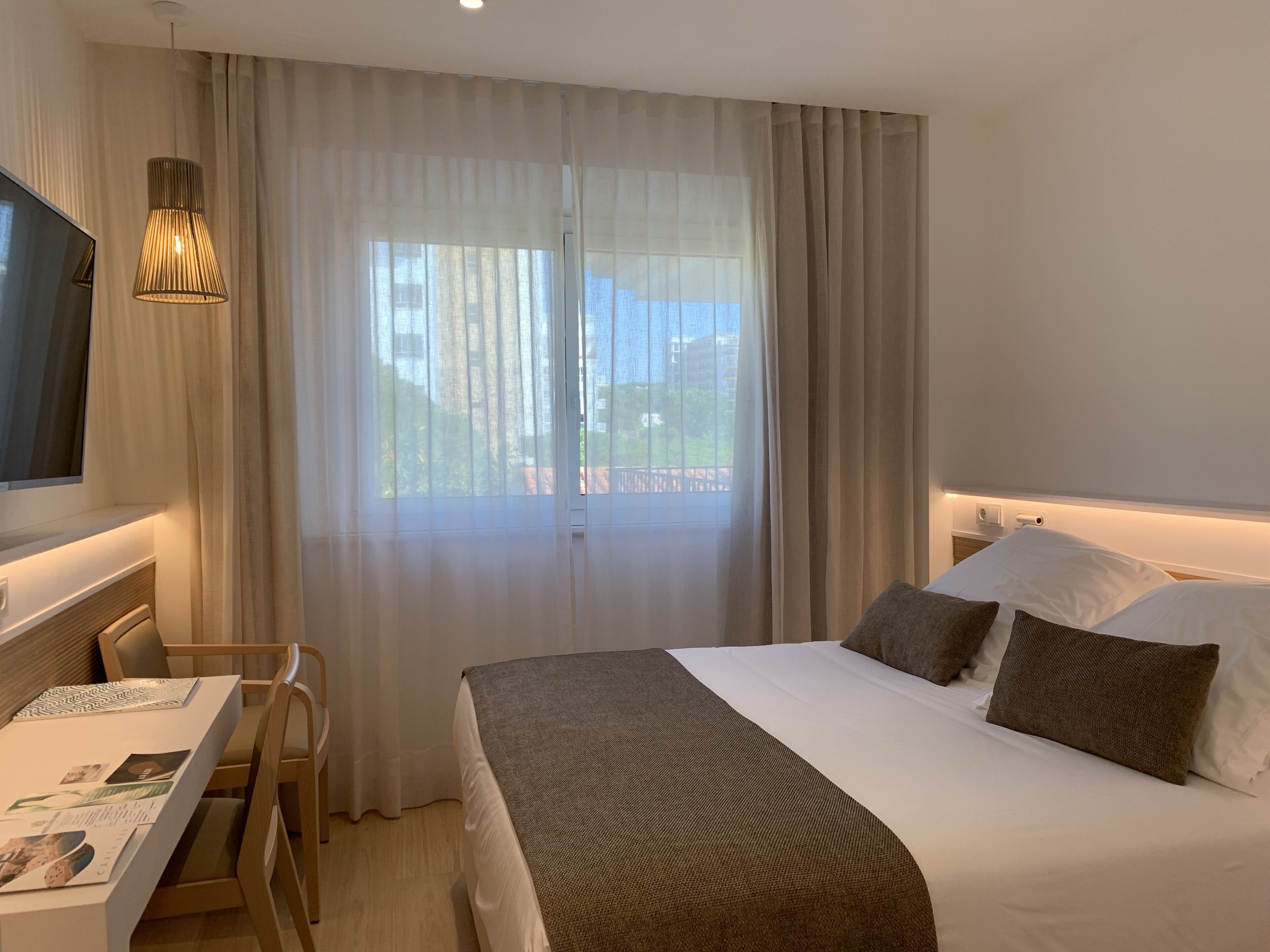 Een hotelkamer met een bed, een bureau, een stoel, een televisie en een raam met gordijnen.
