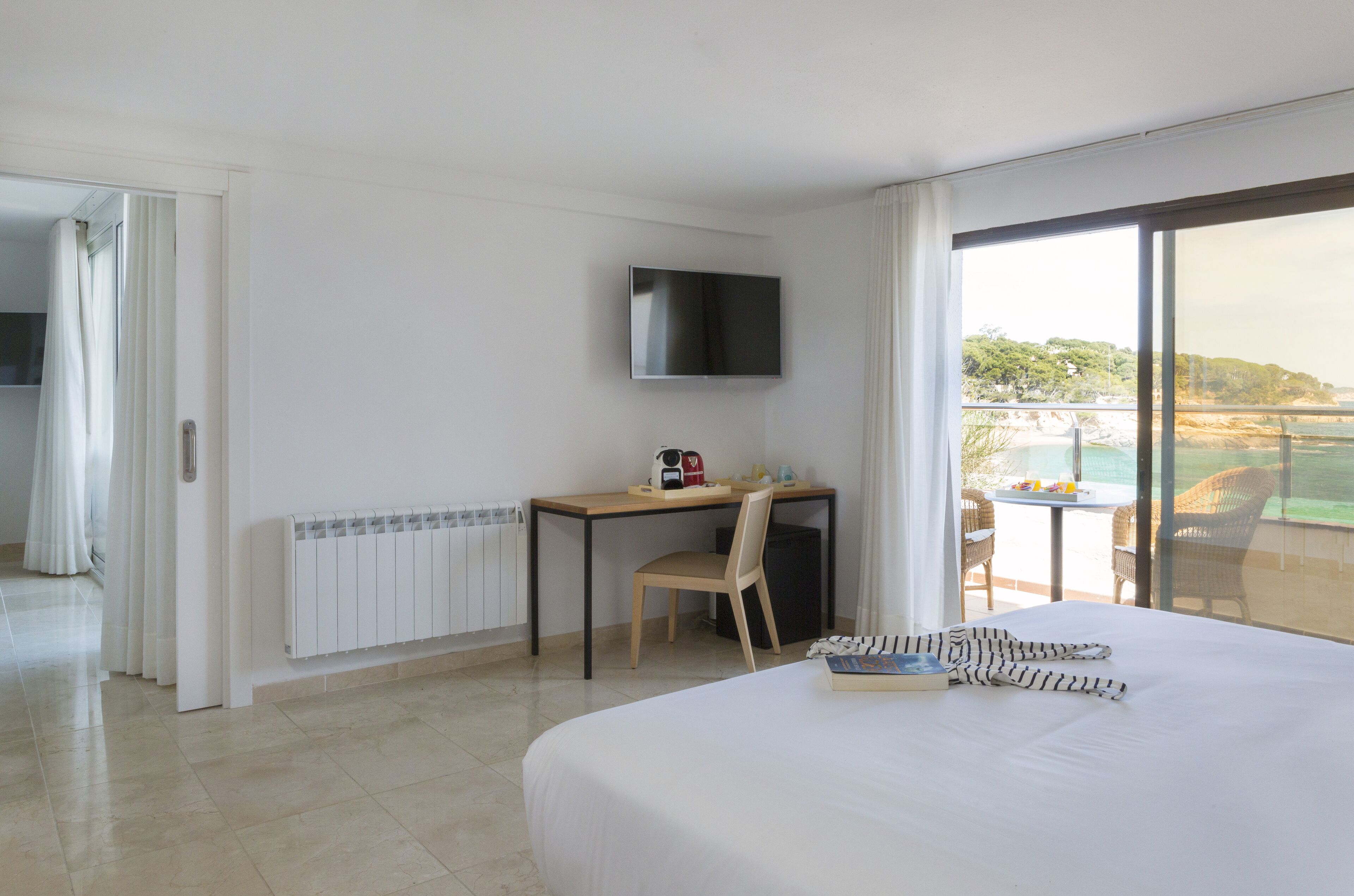 Quarto de hotel com cama, escrivaninha com cadeira, televisão e varanda com vista para o mar.