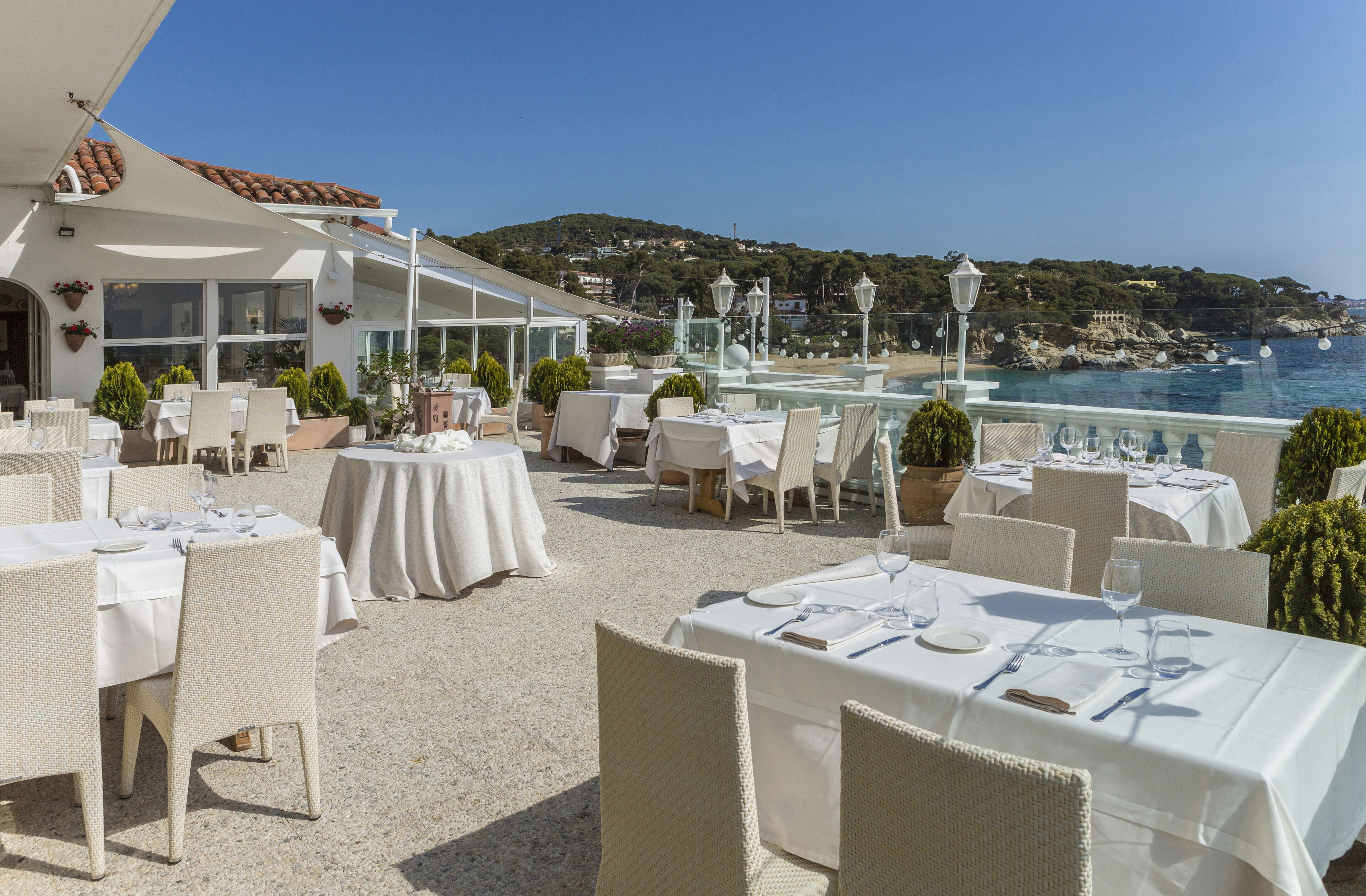 An outdoor dining area with tables set for two, overlooking a coastal view.