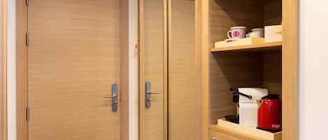 A wooden wardrobe with a sliding door, a shelf with a coffee maker, and a cup.