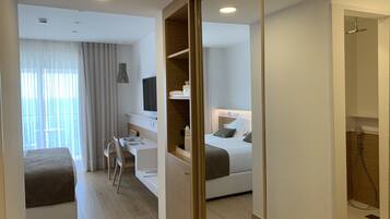 Quarto de hotel moderno com cama, escrivaninha, cadeira, televisão e zona de chuveiro.