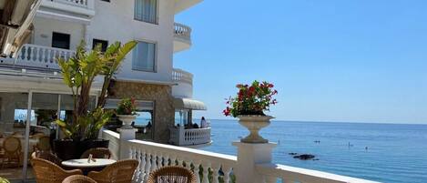 A balcony with wicker furniture, a white railing, and a view of the sea.