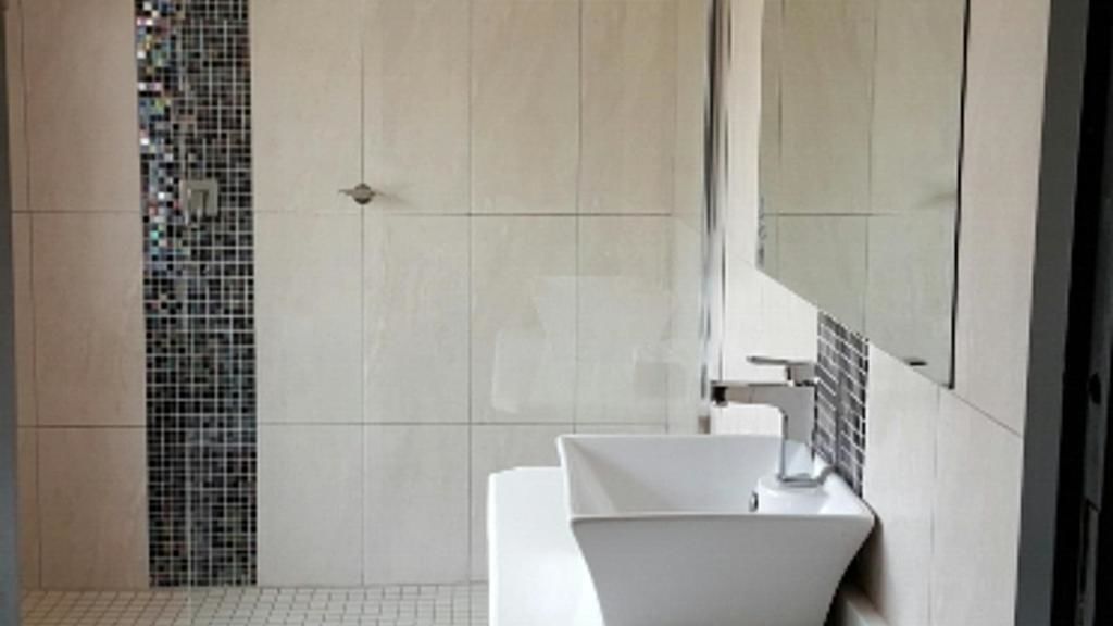 Un baño moderno con un lavamanos blanco, un espejo y una zona de ducha con azulejos.