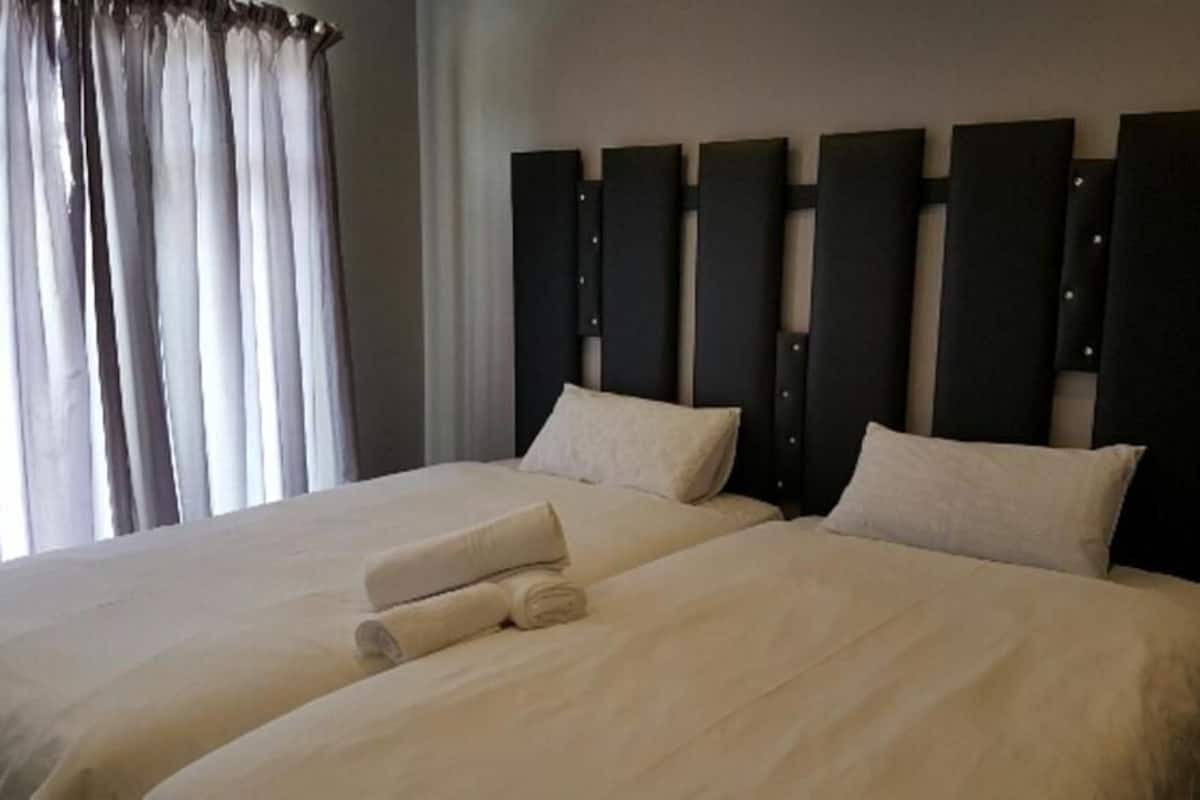 A double bed with a headboard, a window with curtains, and a neatly made bed with a rolled towel.