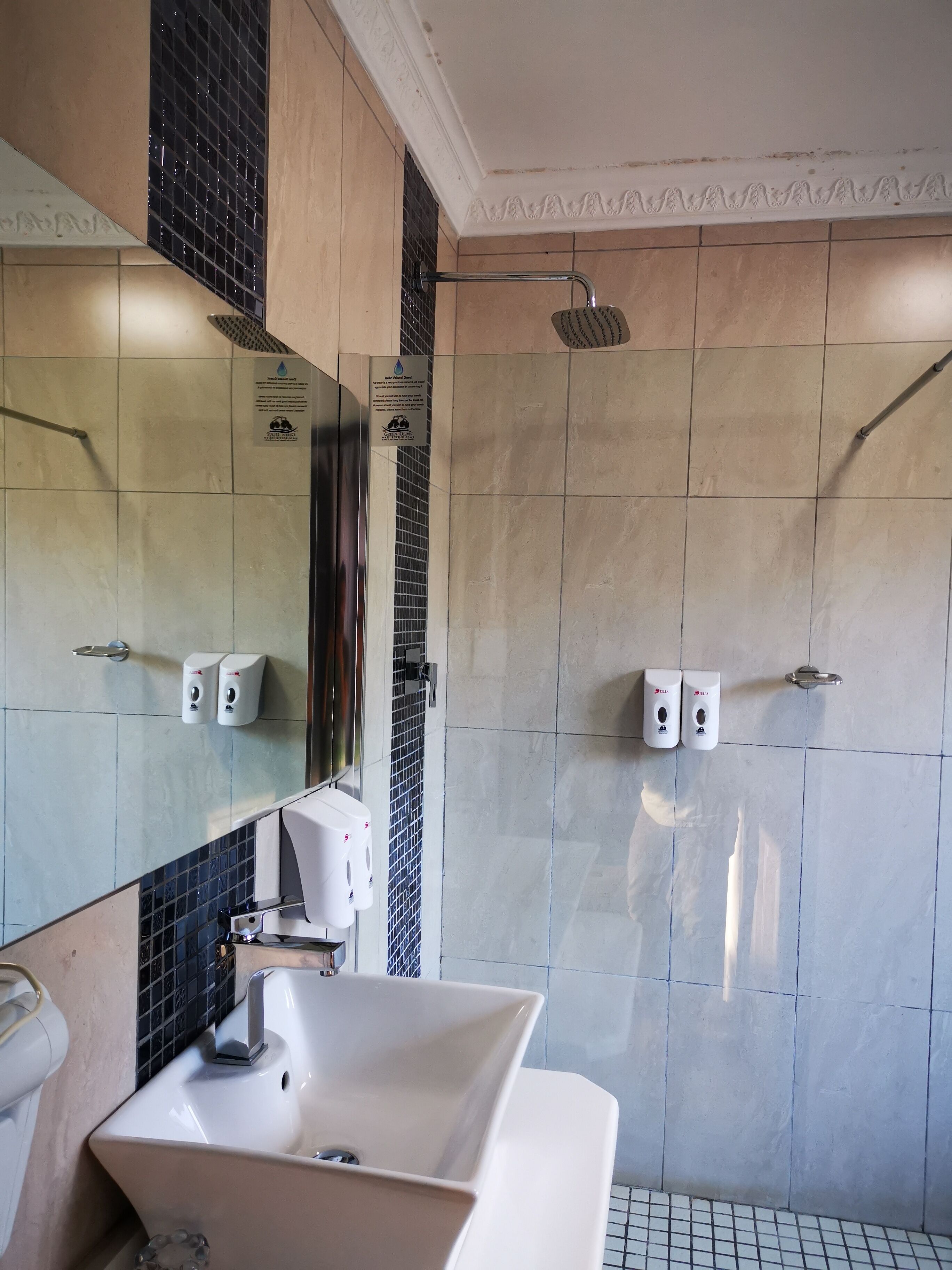 A modern bathroom with a large sink, a mirror, a shower with a handheld showerhead, and hand sanitizer dispensers.