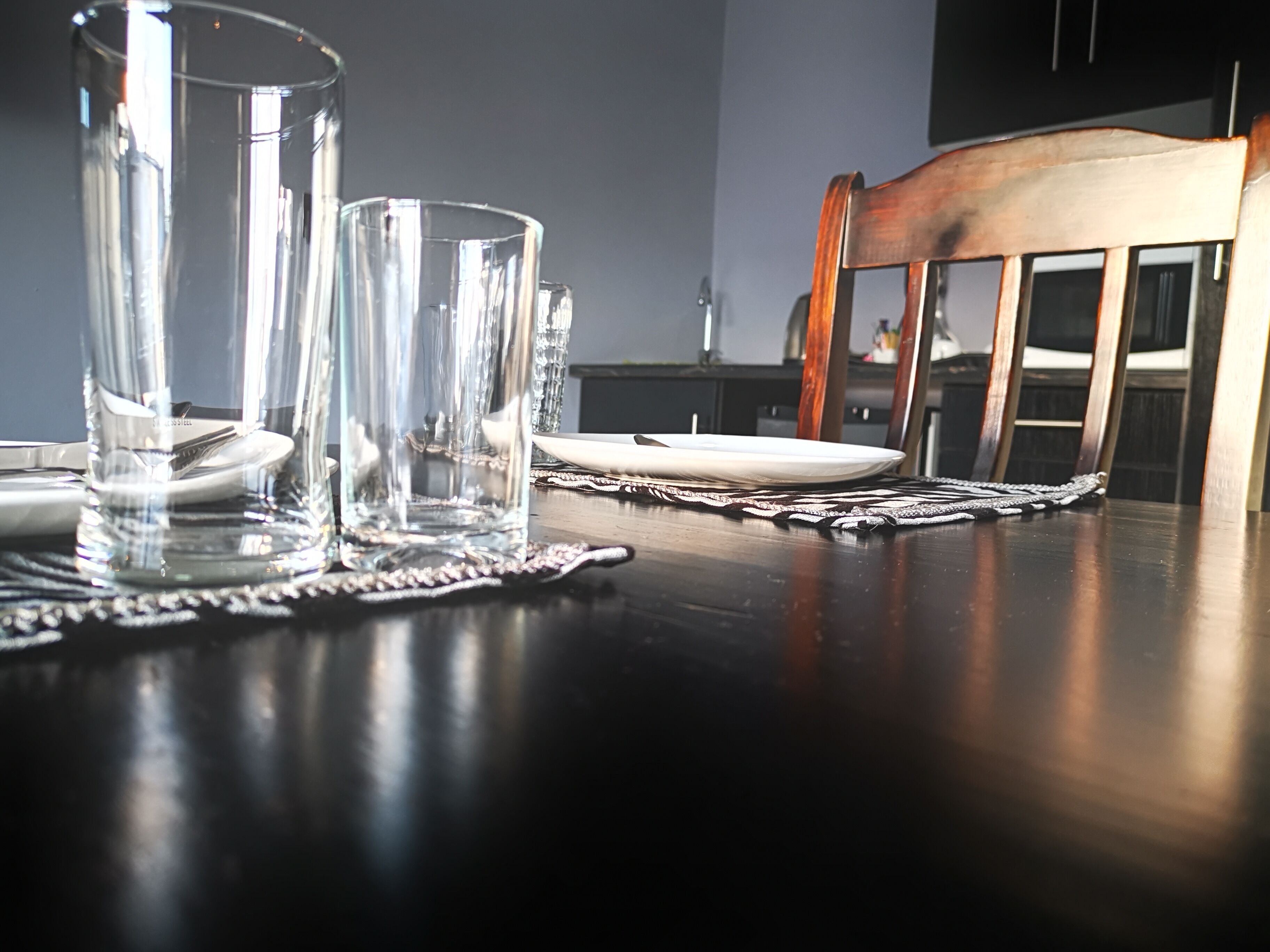 Una mesa de comedor con cristalería transparente y platos, una silla de madera y un mantel individual.