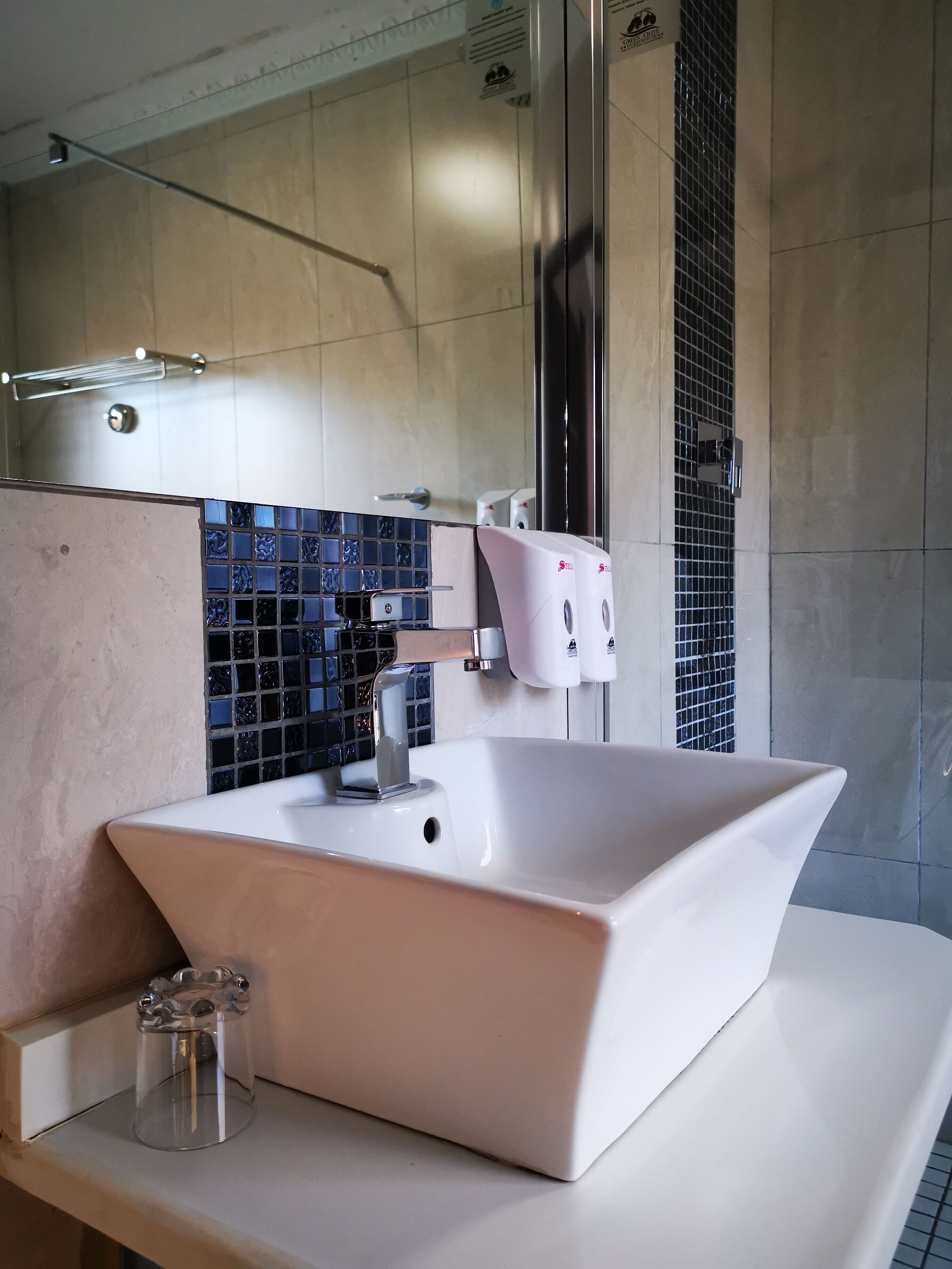 A modern bathroom with a large white sink, a glass shower enclosure, and a tiled backsplash.