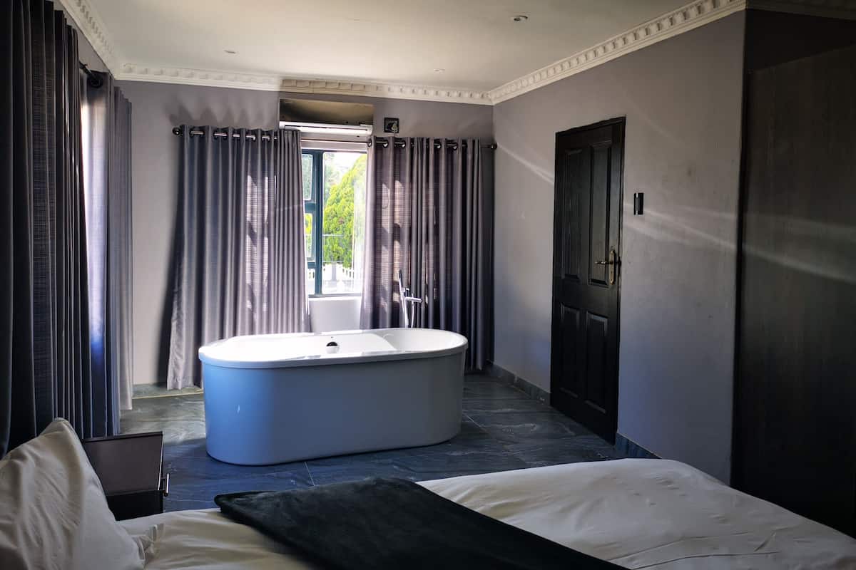 A modern bathroom with a freestanding bathtub, a large window with curtains, and a door to the right.