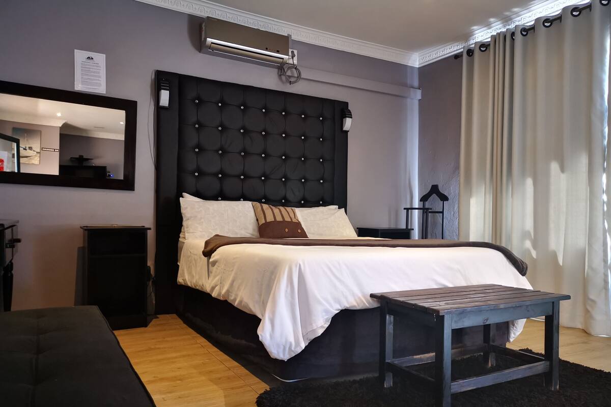 A modern bedroom with a tufted headboard, a bedside table, a mirror, and a window with curtains.