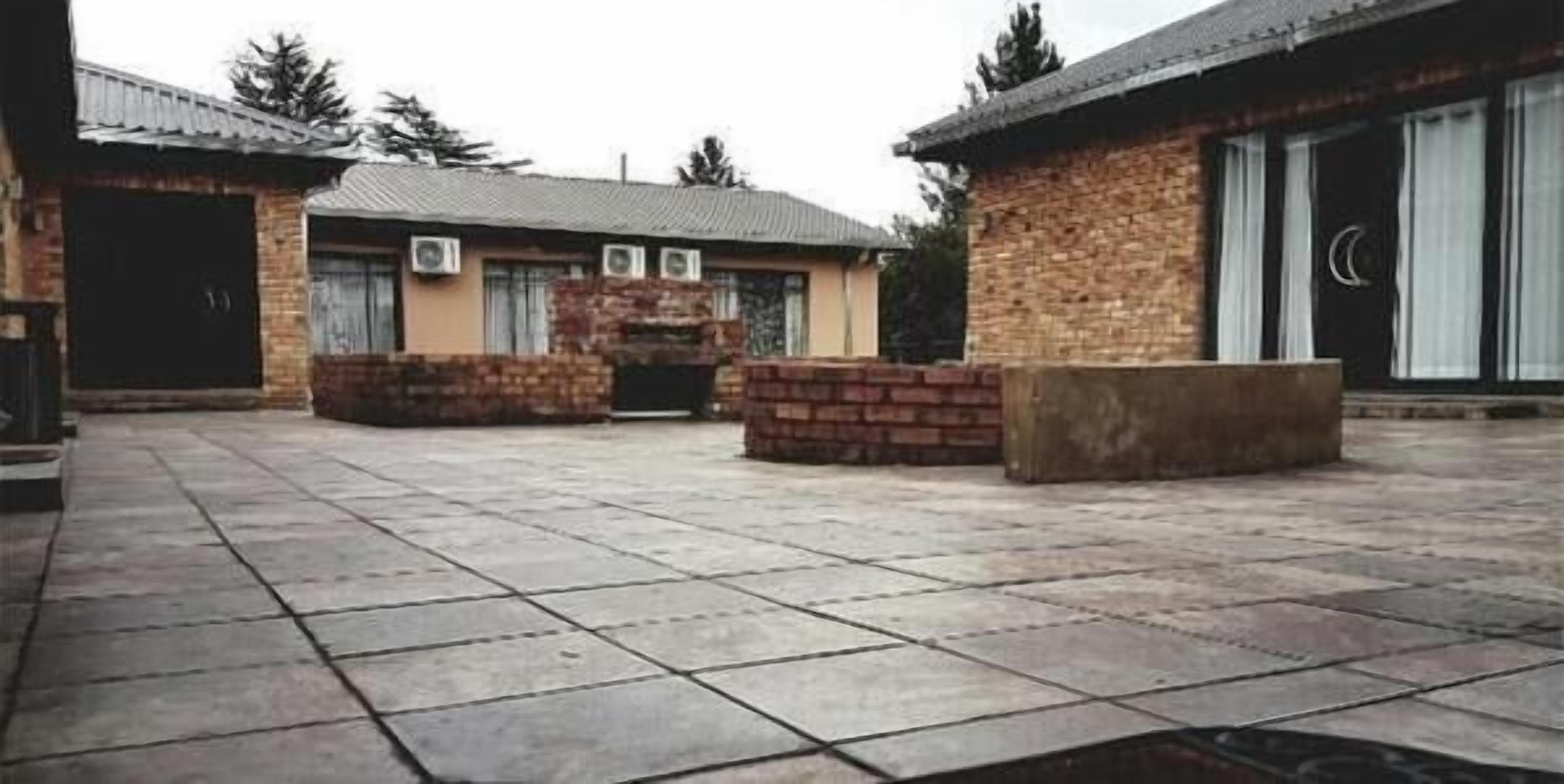 A courtyard with a stone floor, two brick buildings, and a large stone bench.