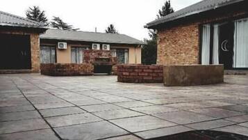 A courtyard with a stone floor, two brick buildings, and a large stone bench.