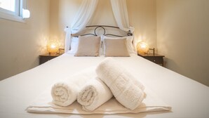 A neatly made bed with white linens and two rolled towels, a canopy bed frame, and bedside lamps on either side.