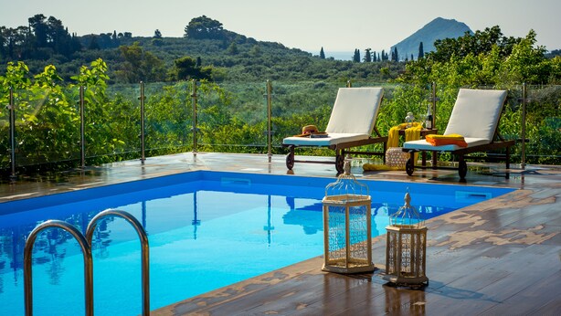 An infinity pool with two sun loungers and decorative lanterns, surrounded by lush greenery and a mountainous backdrop.