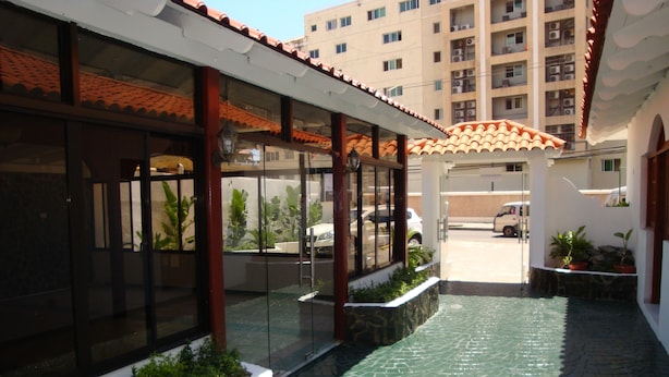 Un espacio exterior techado con suelo de baldosas, puertas de cristal y un edificio con tejado de tejas.
