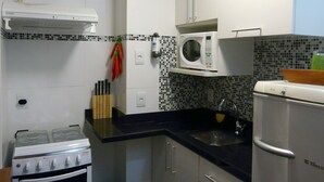 Una cocina compacta con armarios blancos, un microondas, una estufa y un lavamanos.