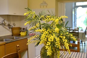 A kitchen with wooden cabinets, a sink, and a vase with yellow flowers on the table. - Villa nei fiori (Florence)