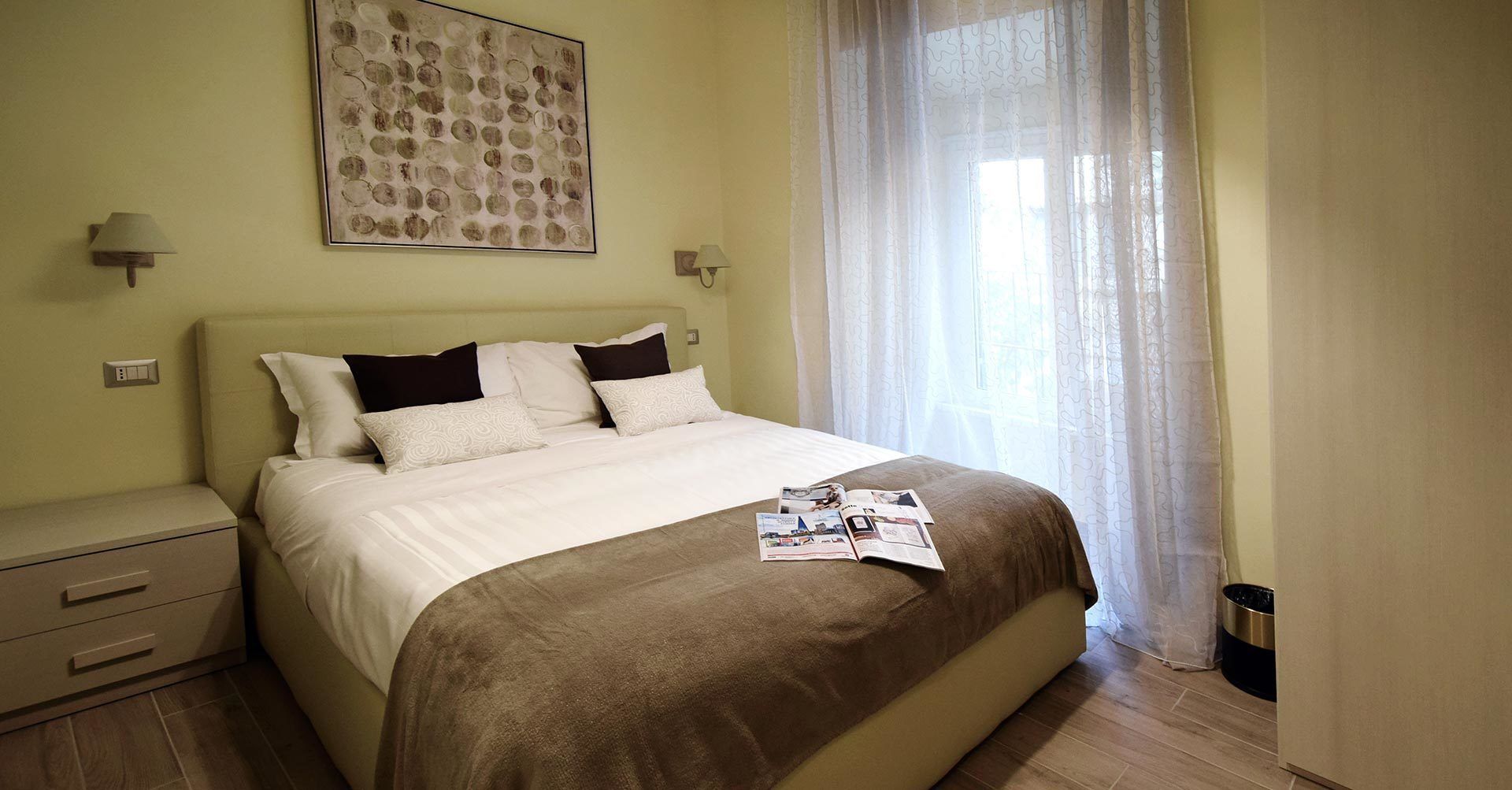 A neatly made bed with a brown blanket, a bedside table with a lamp, and a wall-mounted artwork.