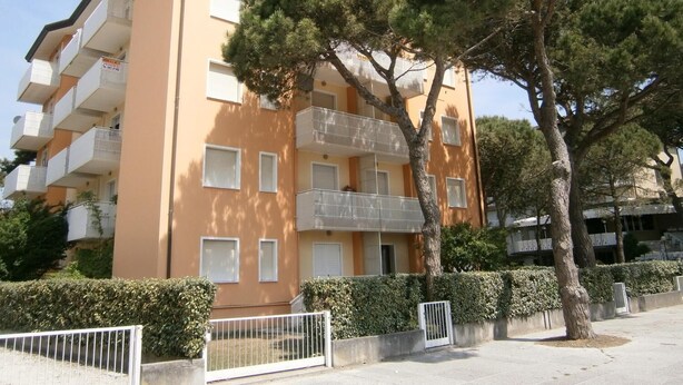 Un immeuble d’appartements à plusieurs étages, doté de balcons, d’une entrée sécurisée et d’une haie bien entretenue.