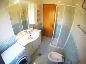 Un baño con lavamanos doble, ducha, inodoro y lavadora.