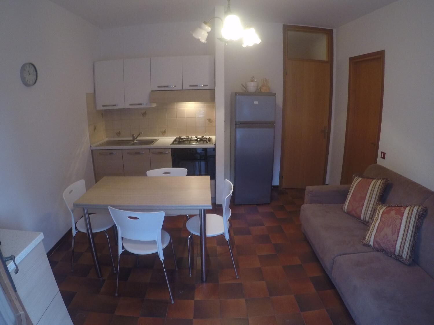 Una cocina compacta con una mesa de comedor y sillas, un refrigerador y un sofá con un cojín estampado.