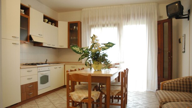 A kitchen with a dining table, chairs, cabinets, a stove, and a television.