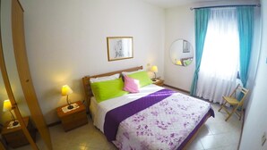 A neatly arranged bedroom with a bed, two bedside tables with lamps, a chair, a mirror, and a window with curtains.