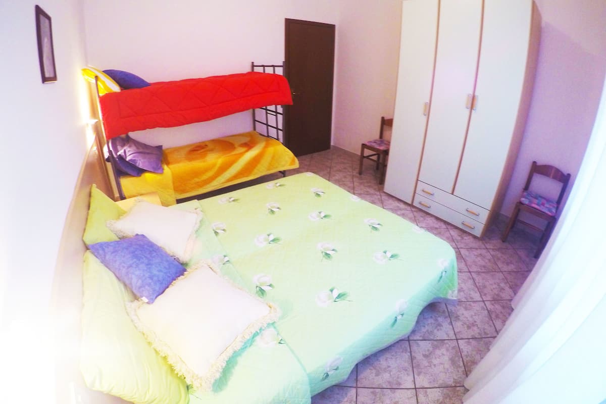 Ein kleines Zimmer mit einem Einzelbett, einem Etagenbett, einem Kleiderschrank und einem Stuhl.