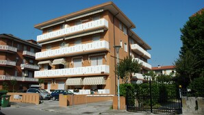 A multi-story residential building with balconies, a gated entrance, and parked cars.