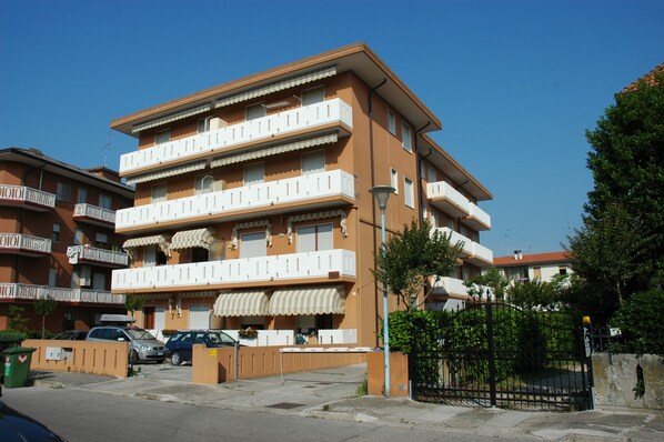 A multi-story residential building with balconies, a gated entrance, and parked cars. - Appartamenti Ponente (Caorle)
