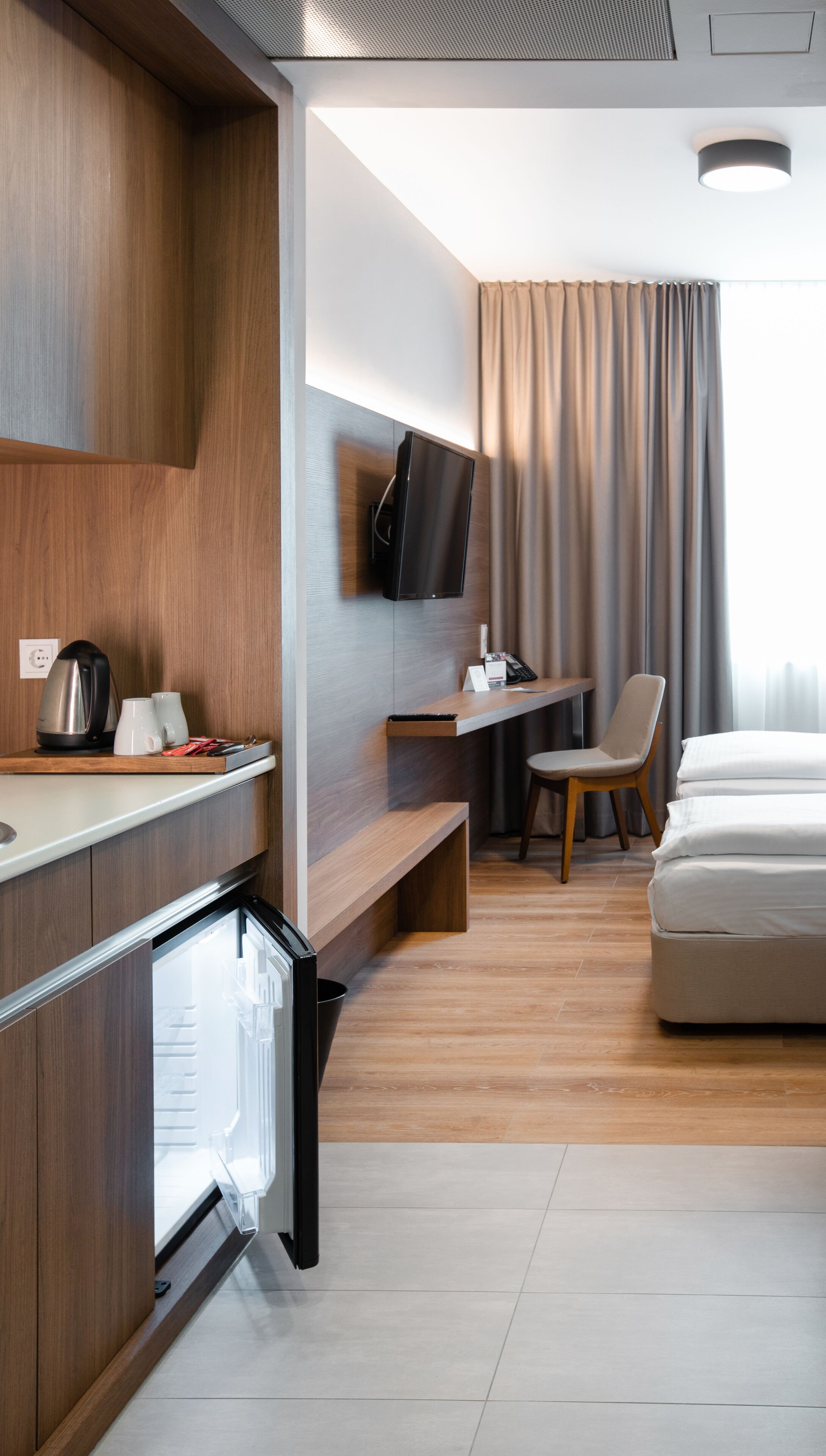 A modern hotel room with a wooden desk, a flat-screen TV, a bed, and a chair.