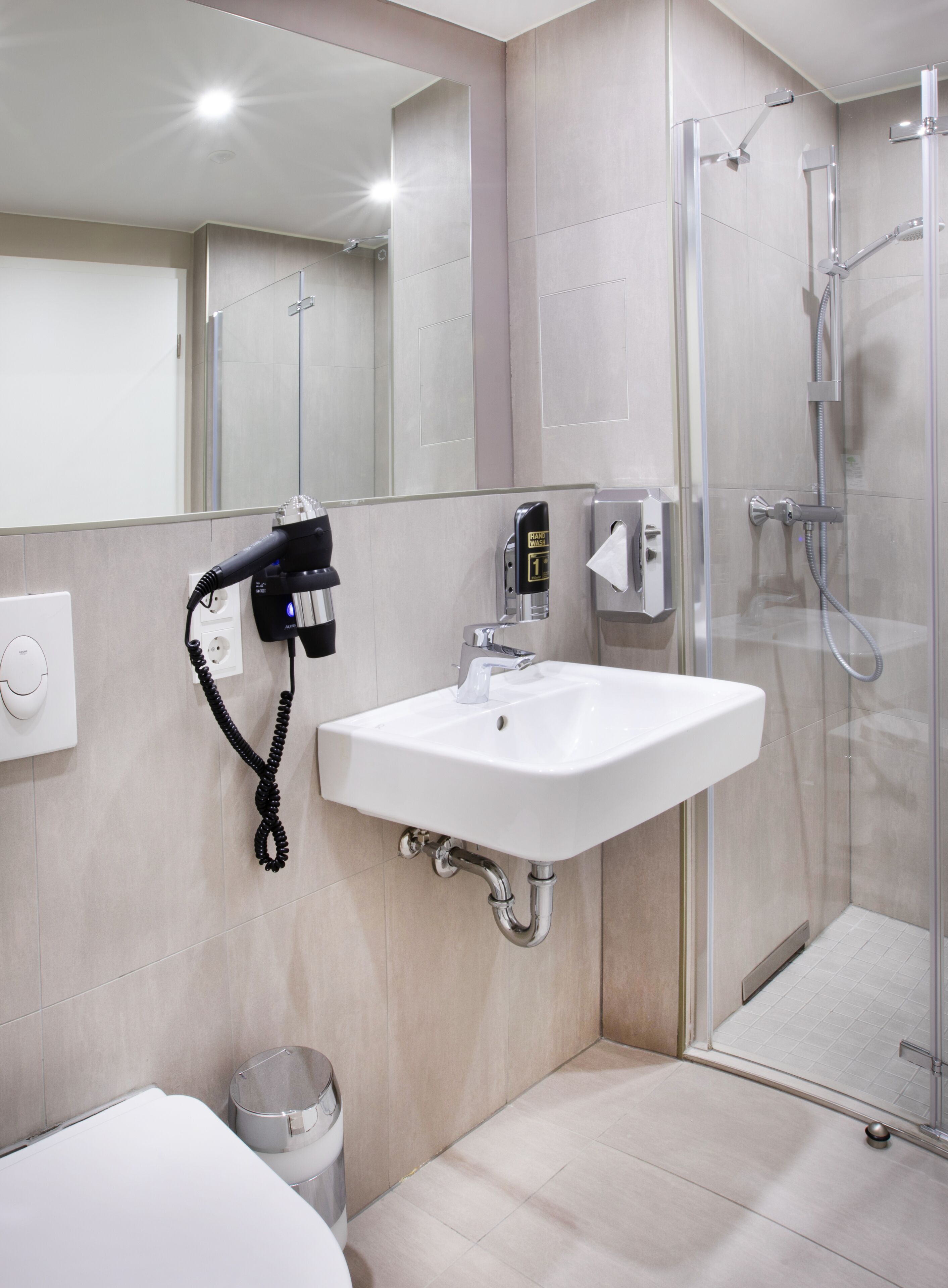 Un baño moderno con lavamanos blanco, secador de pelo de mano, cabina de ducha de vidrio y espejo.