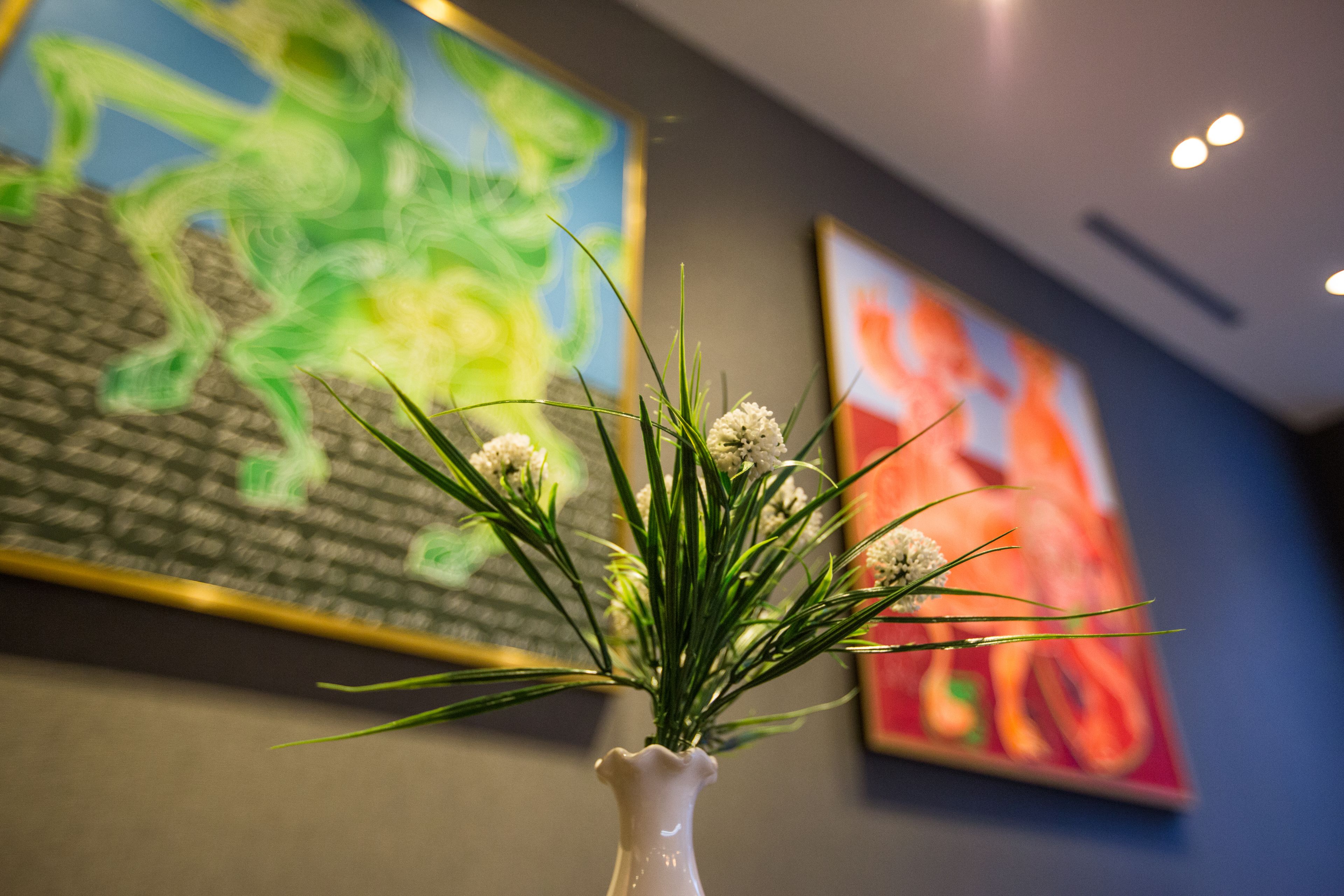 A white vase with green foliage and white flowers on a table.