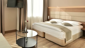 Een moderne hotelkamer met een groot bed, een flatscreen televisie aan de muur, een glazen salontafel en een vaas met bloemen.