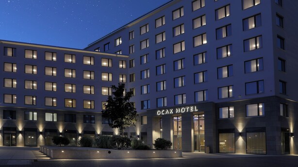 Een modern hotel met meerdere verdiepingen, verlichte ramen en een centrale ingang met het bord 