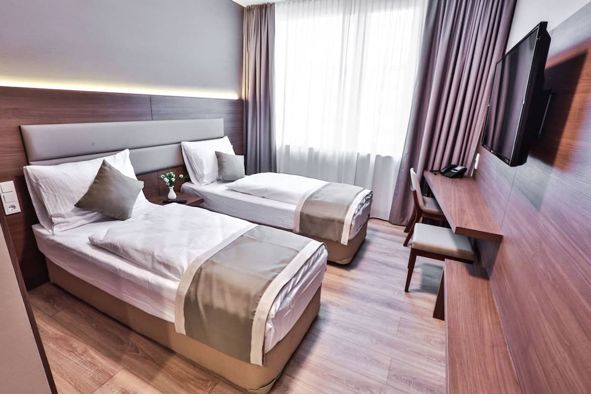 Une chambre d’hôtel avec deux lits, un bureau, une télévision et une fenêtre avec des rideaux.