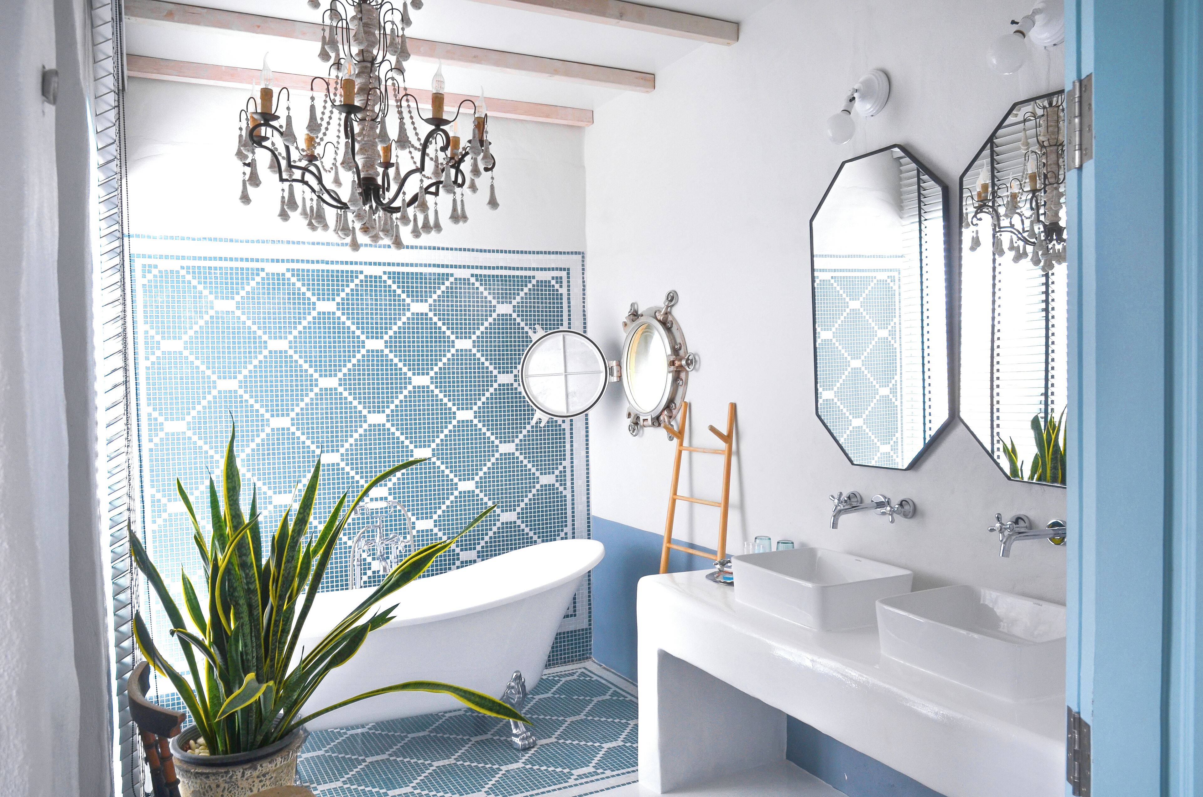 A bathroom with a freestanding bathtub, two sinks, a mirror, and a chandelier.