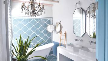 A bathroom with a freestanding bathtub, two sinks, a mirror, and a chandelier.