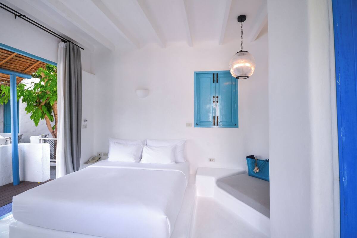 Une chambre d’hôtel avec un lit, une petite table, une armoire bleue et un luminaire suspendu.