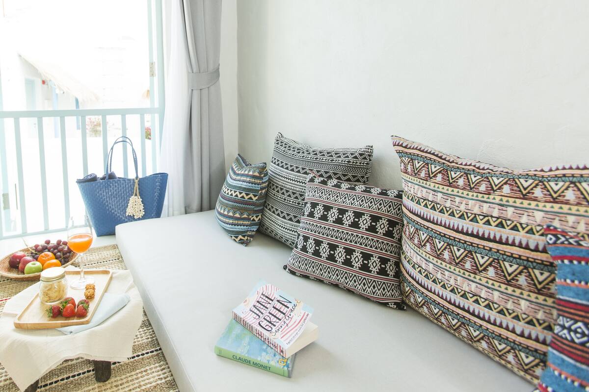 Une chambre à coucher avec un lit, des oreillers, un panier de fruits, un livre et un sac bleu.