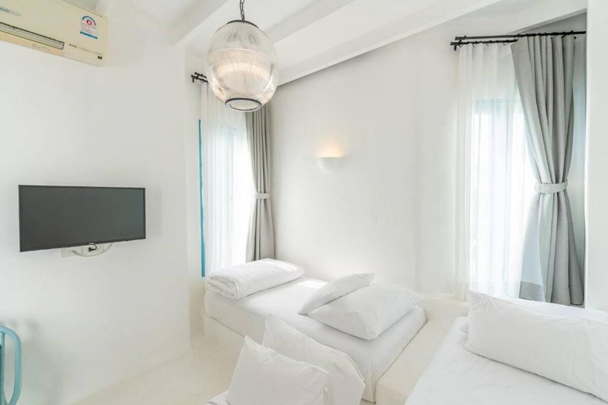 Une chambre moderne dotée d’un téléviseur à écran plat, d’un luminaire suspendu, d’un lit avec une literie blanche et d’une fenêtre avec des rideaux.