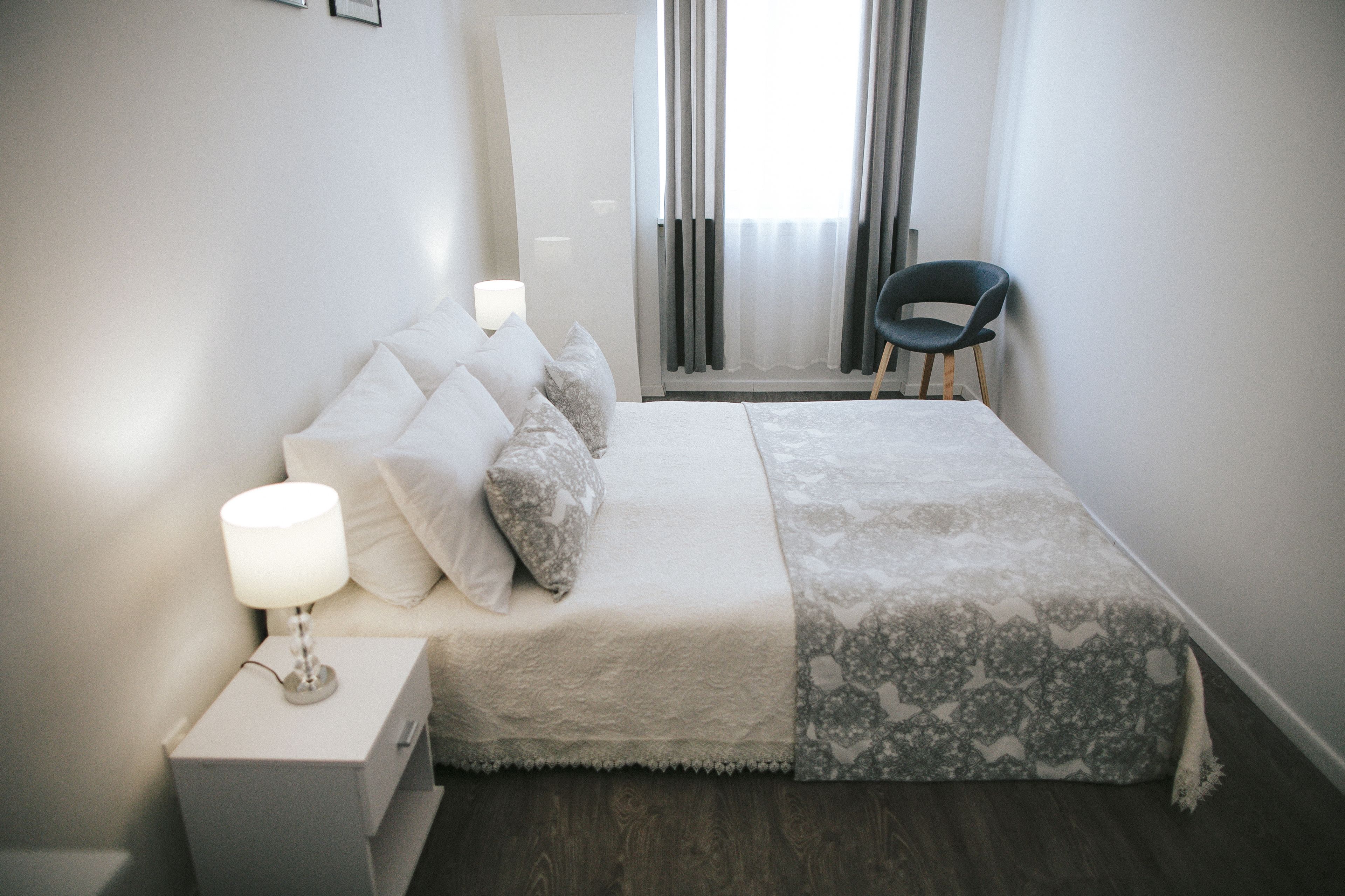 Une chambre bien rangée, avec un lit, des lampes de chevet, une chaise et une fenêtre avec des rideaux.