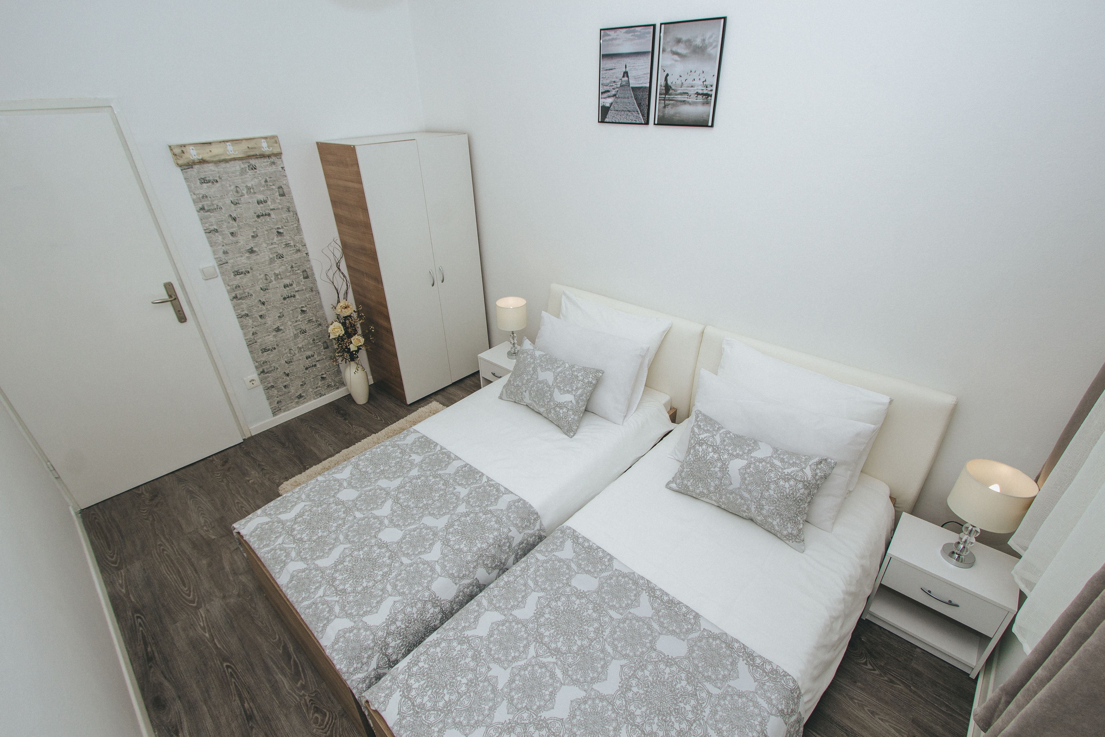 A bedroom with a double bed, two bedside tables, a wardrobe, and a door with a newspaper pattern.